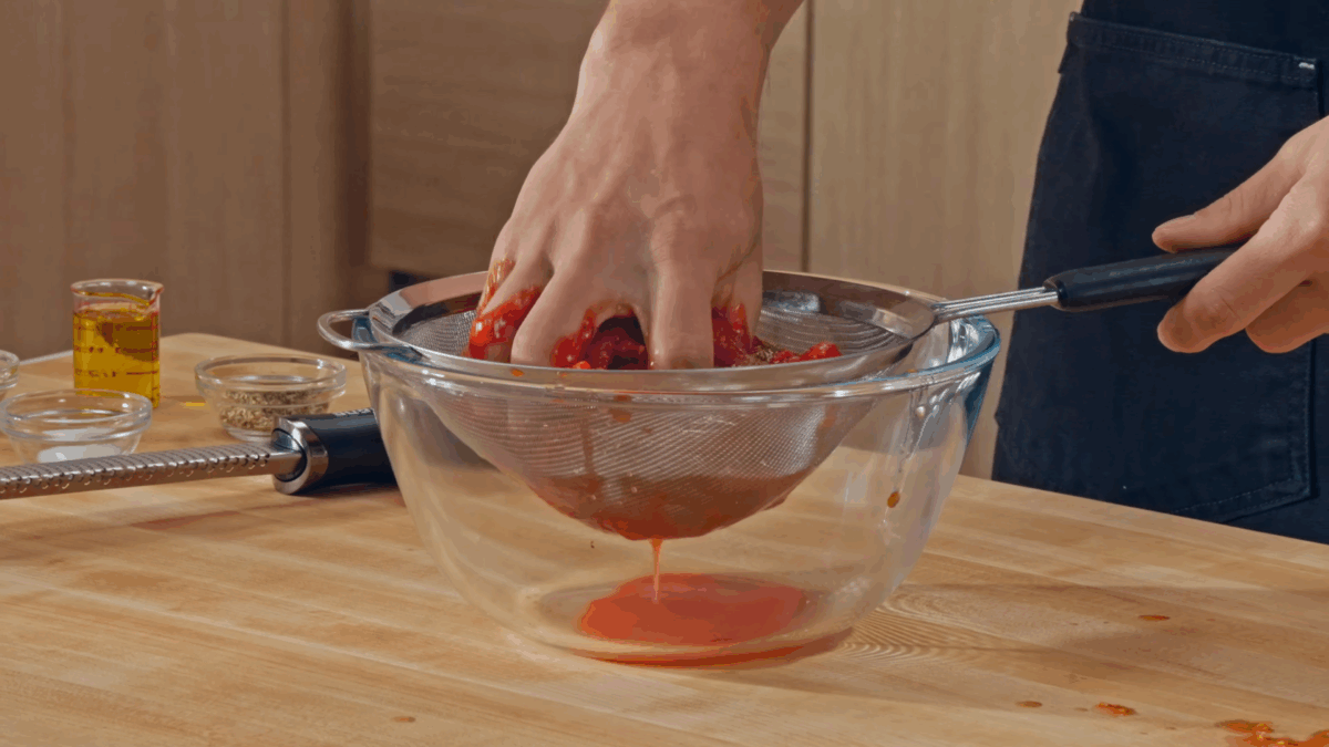 Nick DiGiovanni crushing tomatoes in a strainer over a bowl.