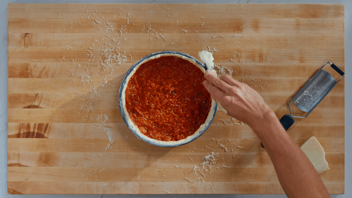 Nick DiGiovanni coating deep dish pizza crust with butter and Parmesan. 