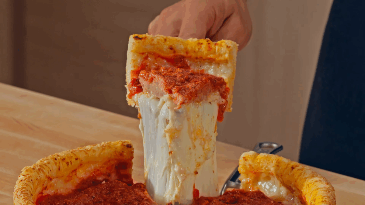 Nick DiGiovanni lifting a slice of deep dish pizza from a full pizza. 