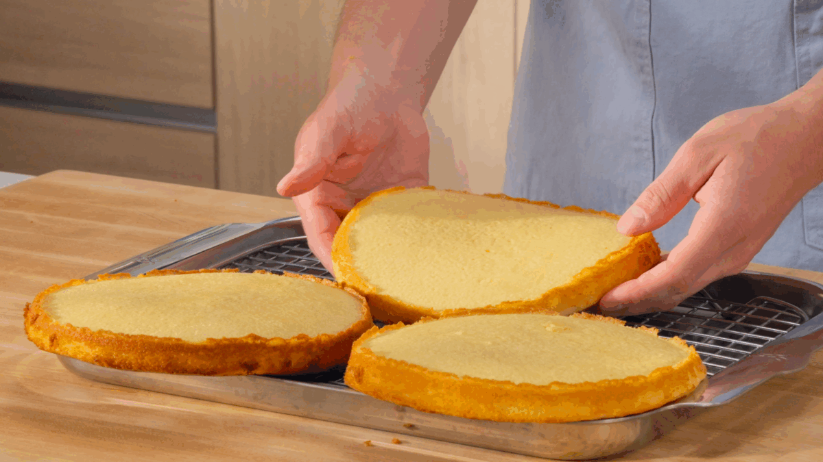 Nick DiGiovanni placing three vanilla cake rounds on a wire rack. 