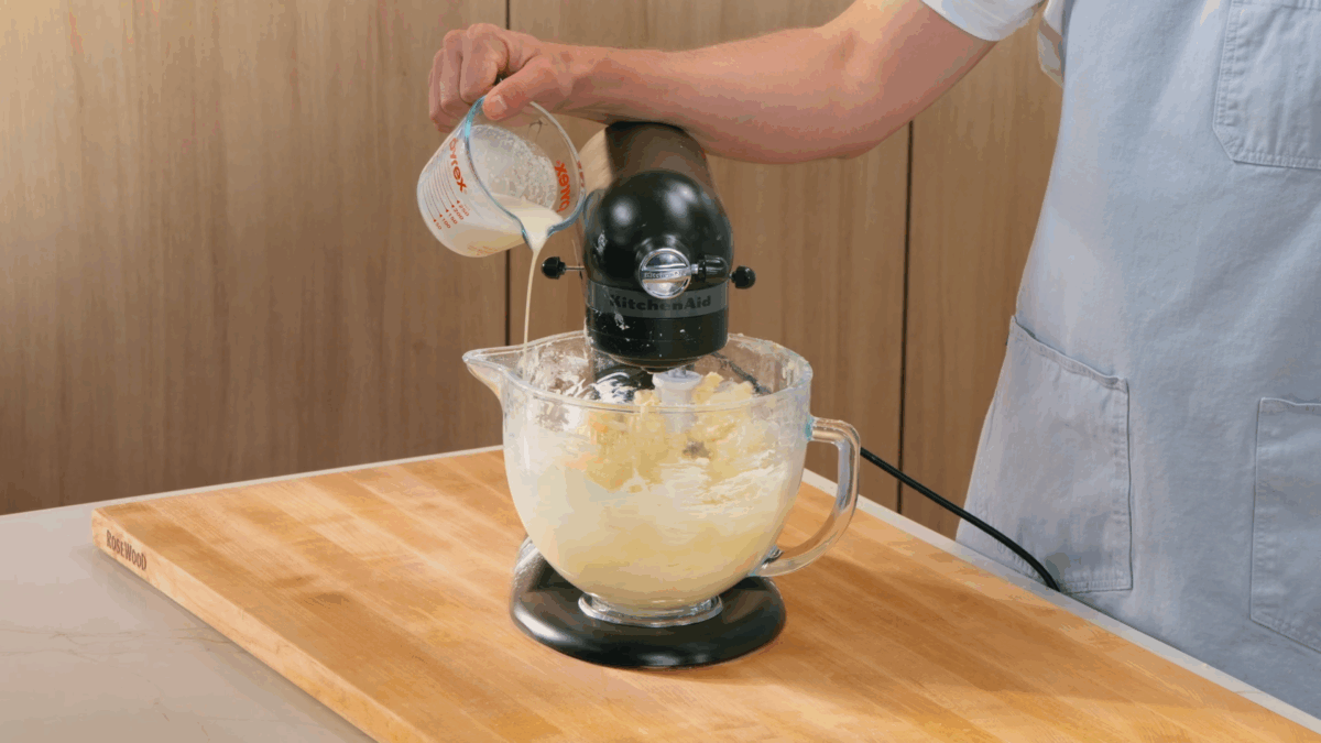 Nick DiGiovanni pouring heavy cream into the bowl of a stand mixer with creamed butter. 