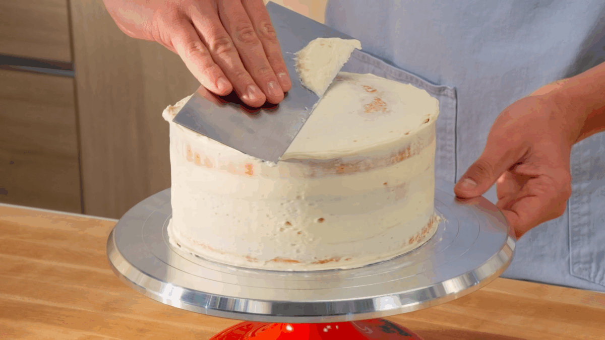 Nick DiGiovanni crumb coating a three-layer vanilla birthday cake on a cake stand. 