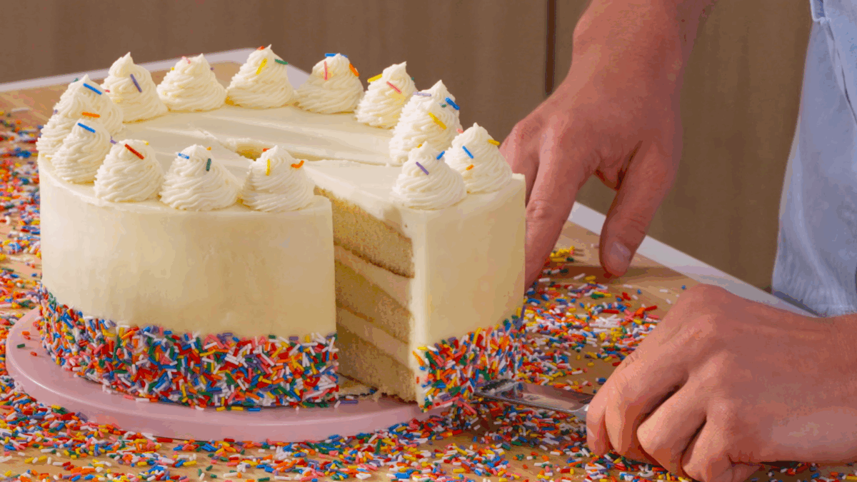 Nick DiGiovanni cutting a slice of vanilla birthday cake from a whole cake. 
