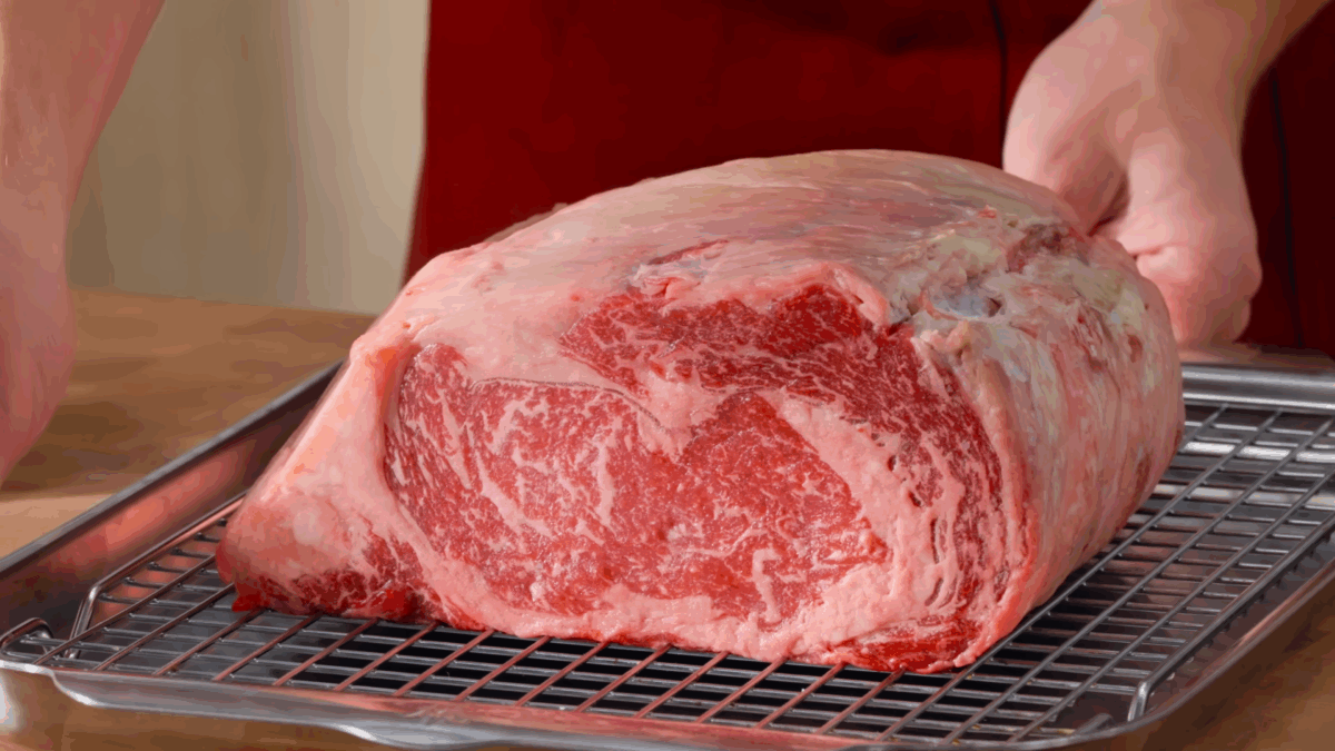 A raw prime rib on a wire rack lined baking sheet.