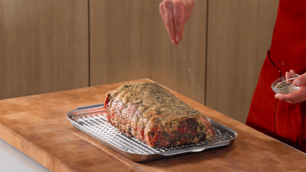 Nick DiGiovanni sprinkling black pepper over a prime rib roast.