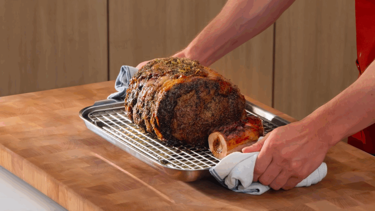 Nick DiGiovanni holding a baking sheet with a cooked prime rib roast and beef marrow bones.