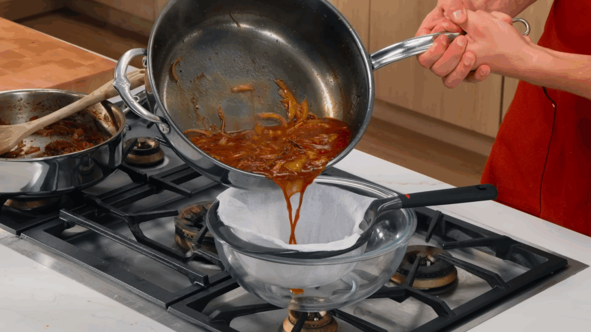 Nick DiGiovanni pouring au just sauce through a fine-mesh sieve.