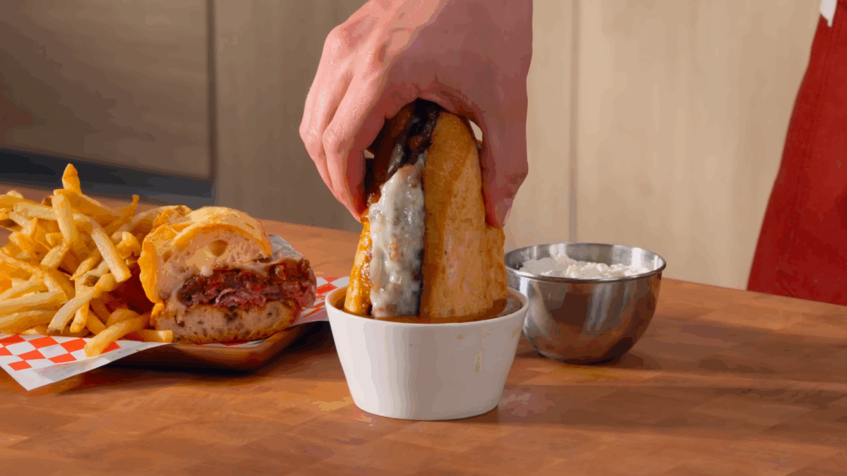Nick DiGiovanni dunking half a French dip sandwich into a bowl of au jus.