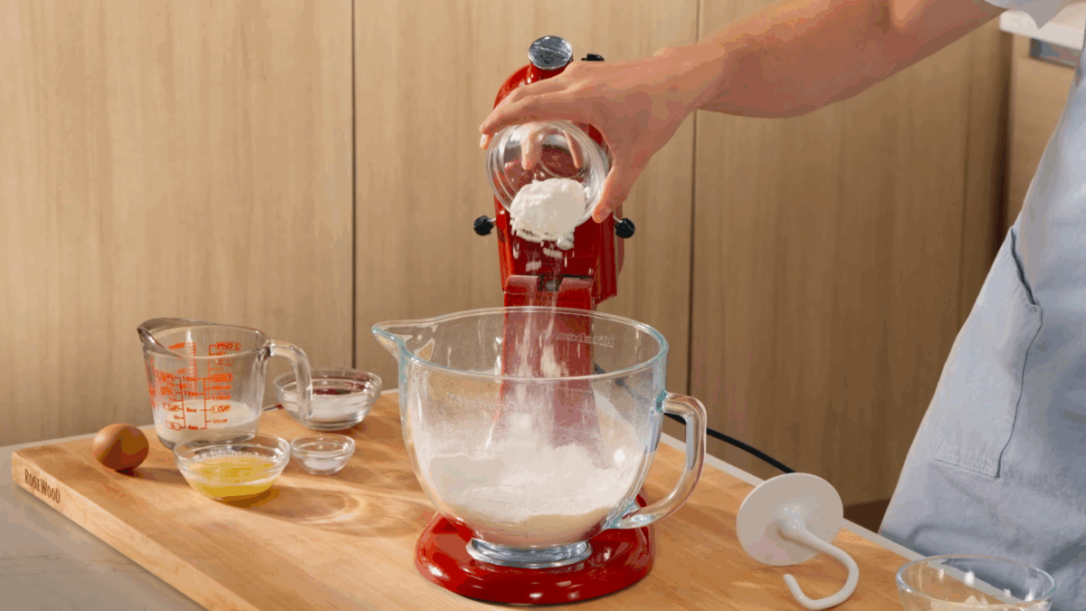 Nick DiGiovanni combining bread dough ingredients in the bowl of a stand mixer fitted with a dough hook. 