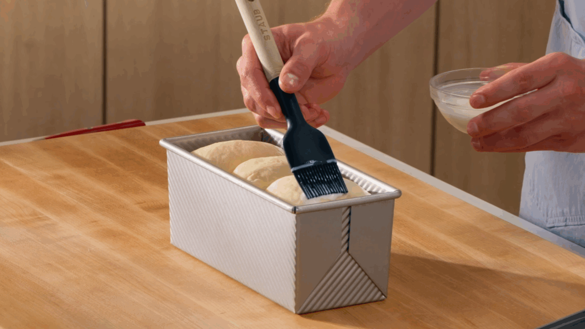 Nick DiGiovanni brushing milk over a raw shokupan loaf in a pan. 