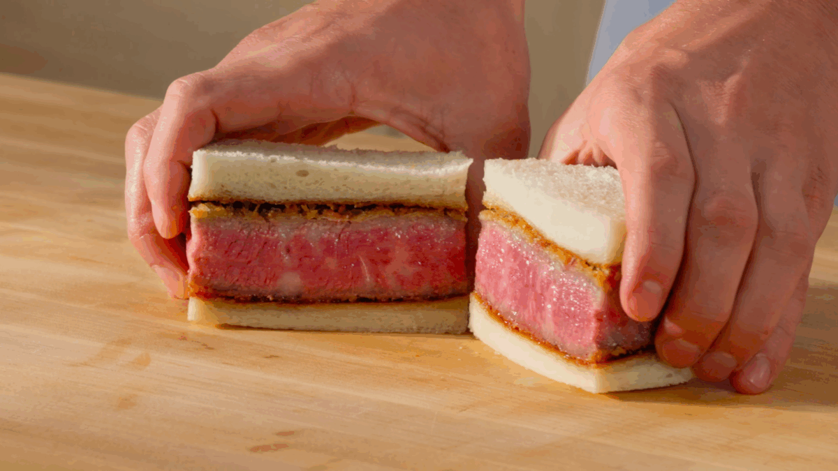 Nick DiGiovanni holding two halves of a Wagyu katsu sando. 