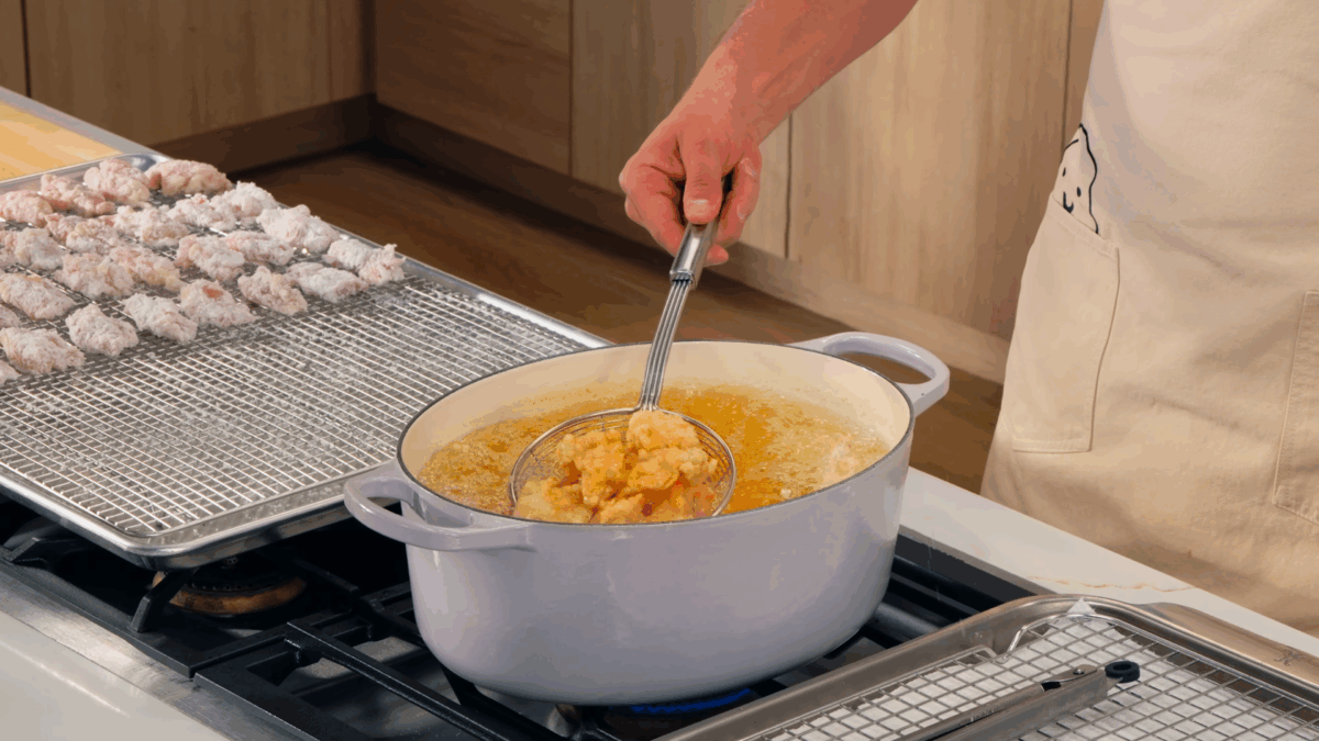 Nick DiGiovanni lifting fried chicken pieces from a pot of oil with a spider.