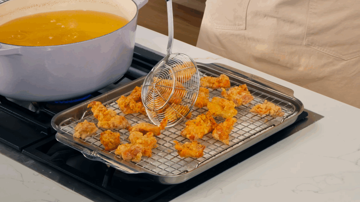 Nick DiGiovanni transferring fried chicken pieces to a wire rack.