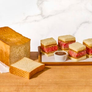 Wagyu katsu sando pieces on a platter next to a loaf of Japanese milk bread.