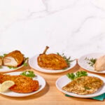 Five plates of chicken breasts prepared five different ways.