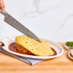 Nick DiGiovanni slicing into the omelet of plated omurice.