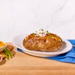 A baked potato on a plate topped with sour cream, chives, and bacon.