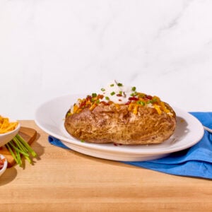 A baked potato on a plate topped with sour cream, chives, and bacon.