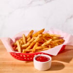 A basket of homemade french fires with a bowl of ketchup on the side.