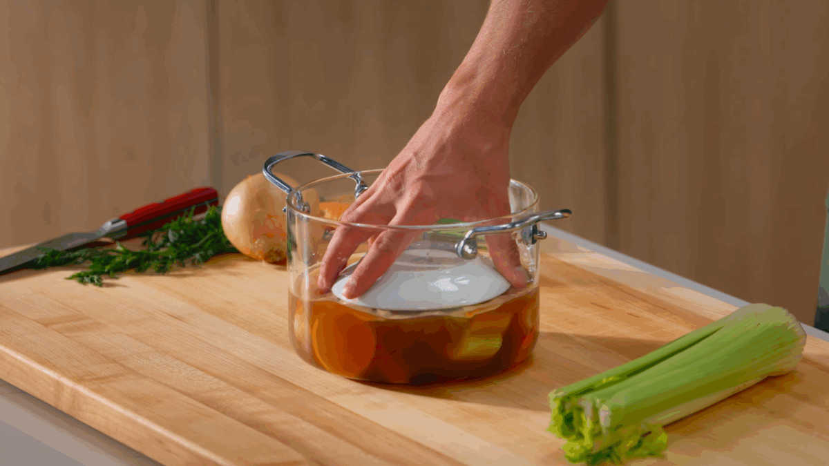 Nick DiGiovanni placing a plate over chicken in a pot of broth.