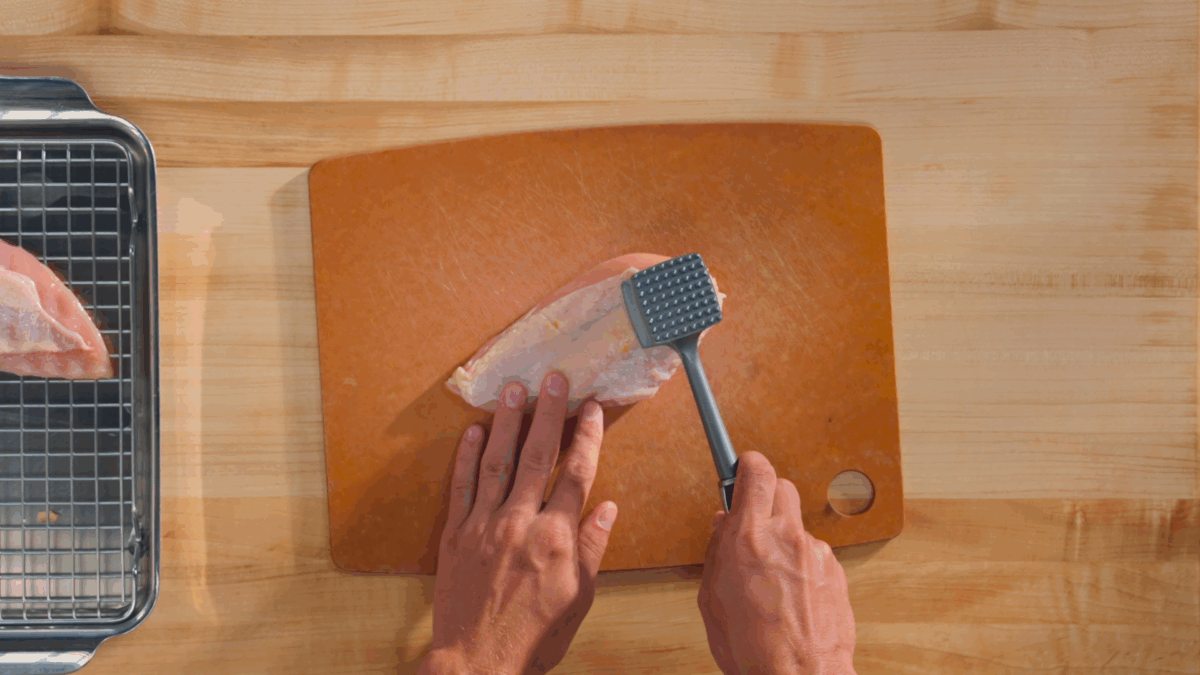 Nick DiGiovanni using a meat mallet to pound a chicken breast on a cutting board.