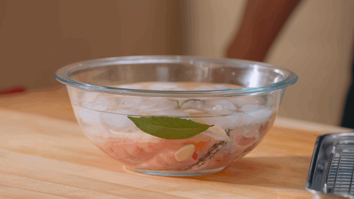 Raw chicken submerged in a bowl of brine.