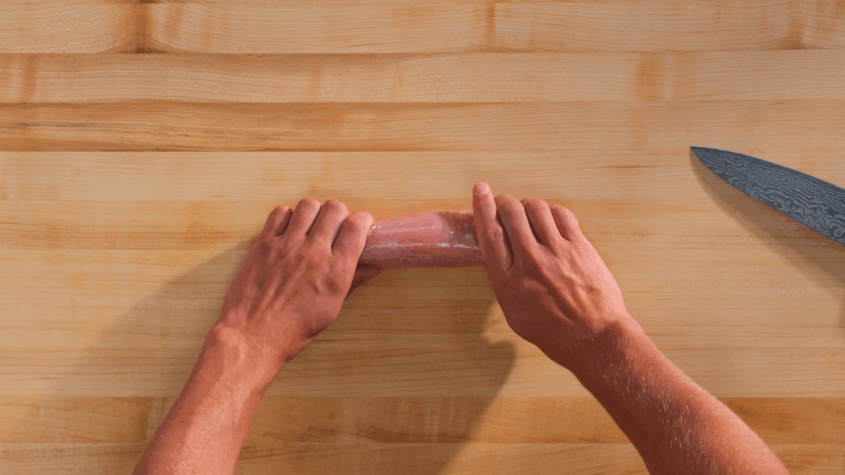 Nick DiGiovanni using plastic wrap to wrap a stuffed chicken breast into a cylinder.