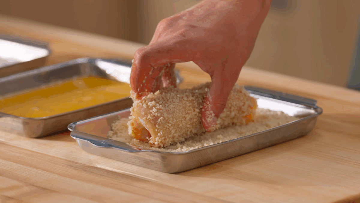 Nick DiGiovanni breading a raw stuffed chicken breast.