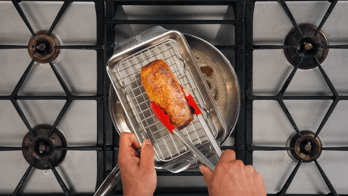 Nick DiGiovanni transferring a seared stuffed chicken breast to a wire rack.