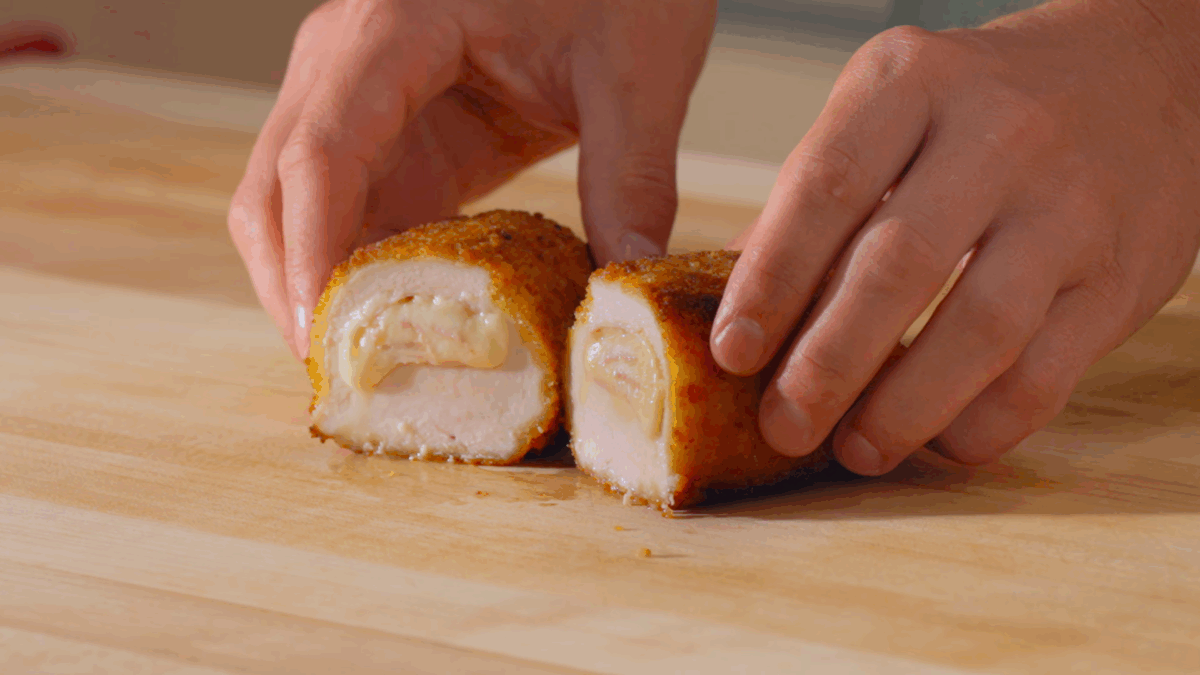 Nick DiGiovanni pulling apart two halves of a sliced ham and cheese stuffed chicken breast.