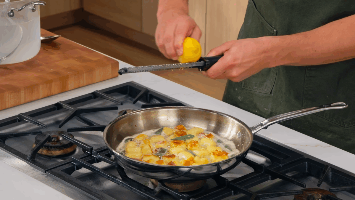 Nick DiGiovanni zesting a lemon over a skillet of homemade gnocchi. 