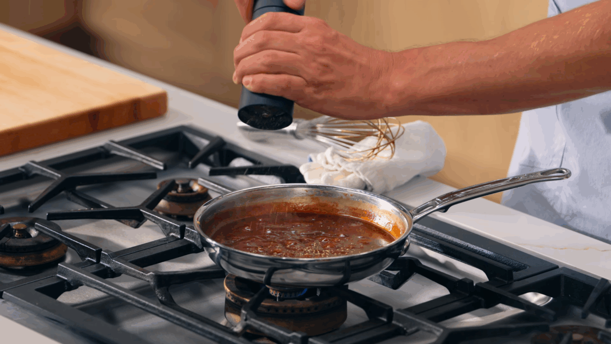 Nick DiGiovanni adding black pepper to a pan of demi-glace for omurice. 