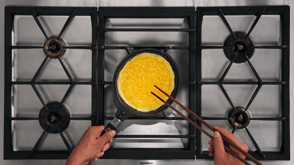 Nick DiGiovanni cooking beaten eggs in a skillet with chopsticks. 