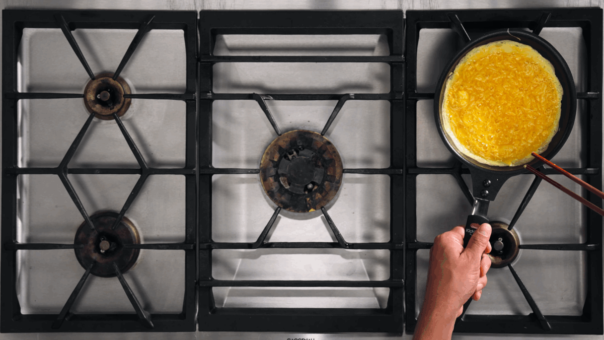 Nick DiGiovanni removing a skillet of partially cooked eggs from the heat source. 