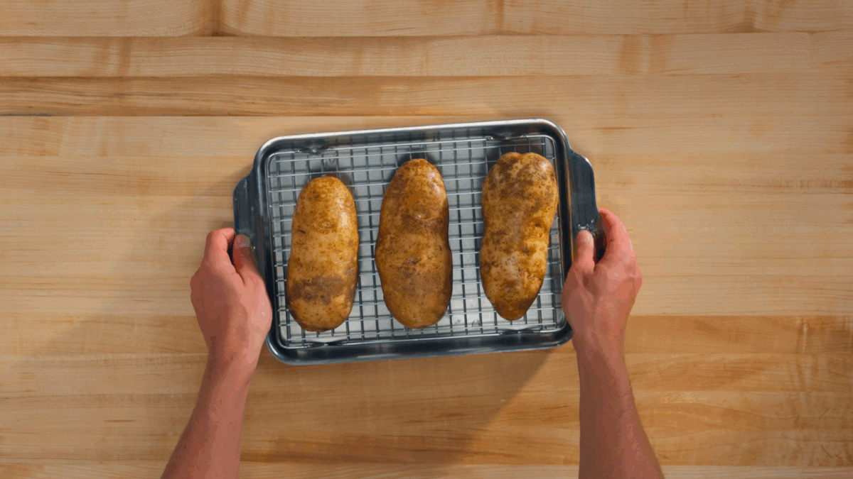 Nick DiGiovanni holding a baking sheet with three baked potatoes. 