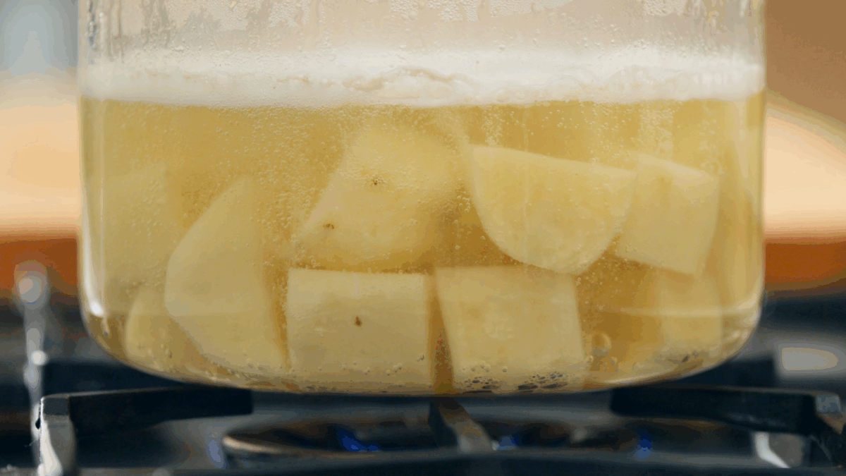 Peeled potatoes boiling in a pot of water on the stovetop. 