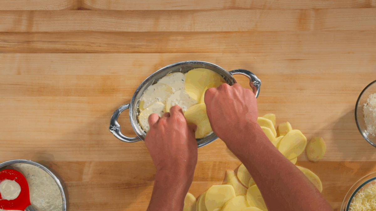 Nick DiGiovanni layering potatoes and cream sauce in a baking dish. 