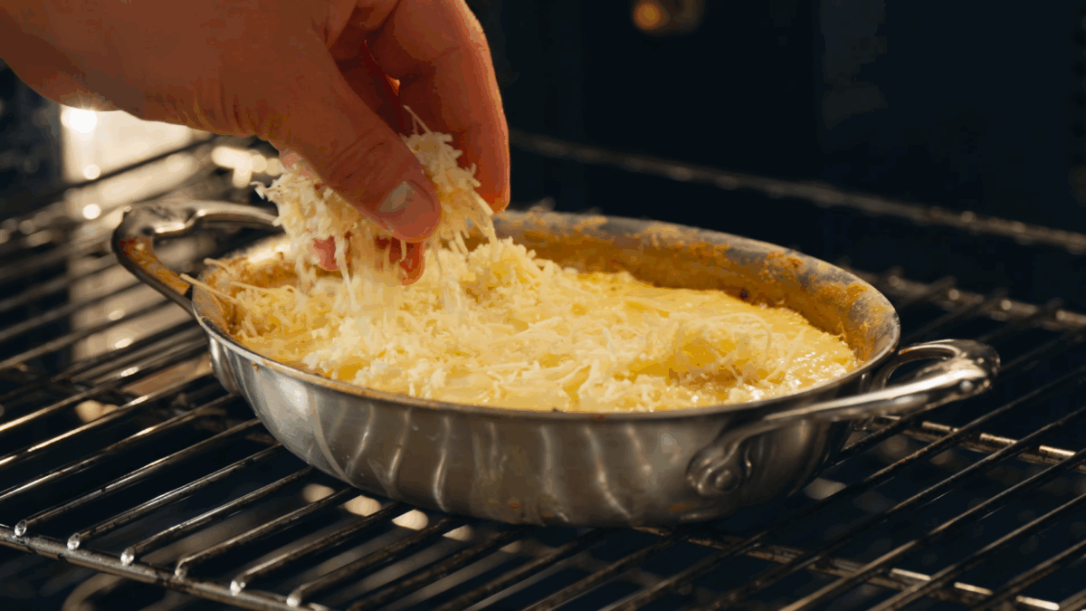 Nick DiGiovanni sprinkling cheese over potato gratin in the oven. 
