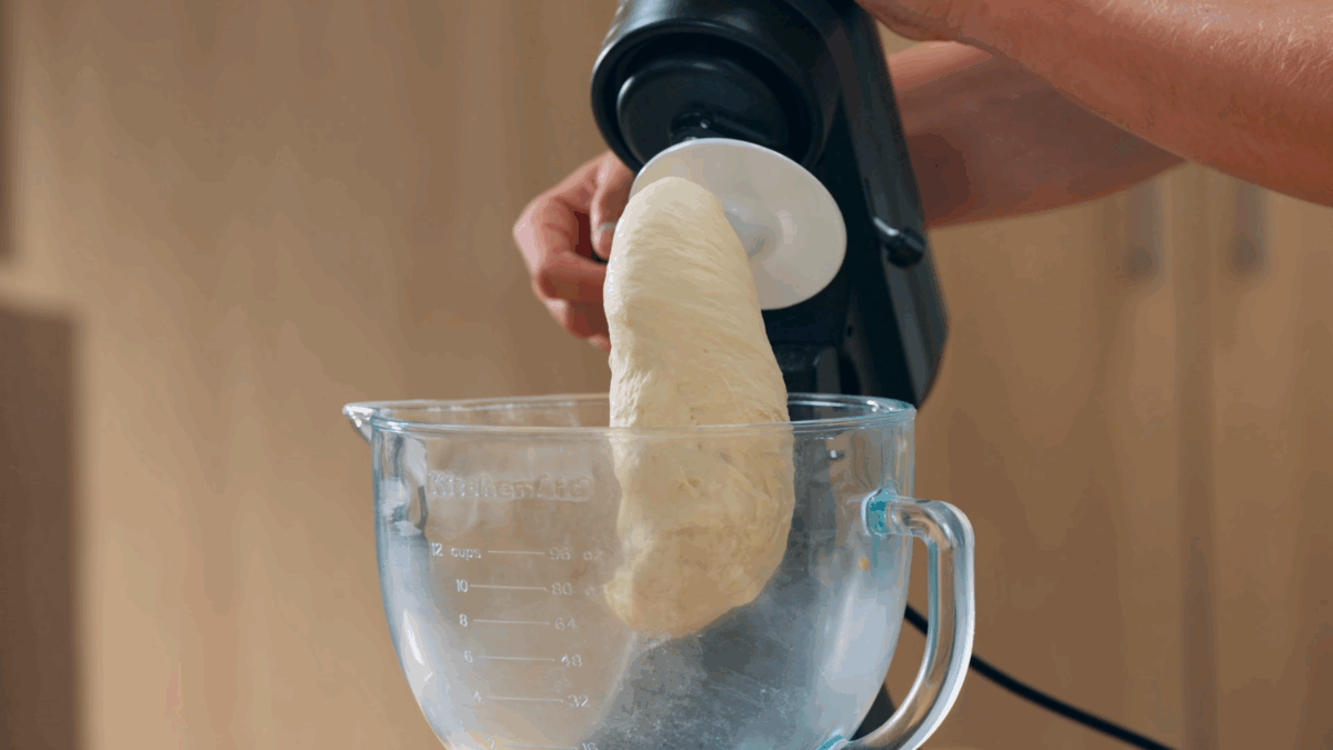 Bahn mi bread dough hanging off the bread hook of a stand mixer. 