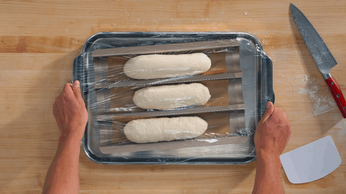 Nick DiGiovanni holding a baguette tray with three proofed bahn mi baguettes.