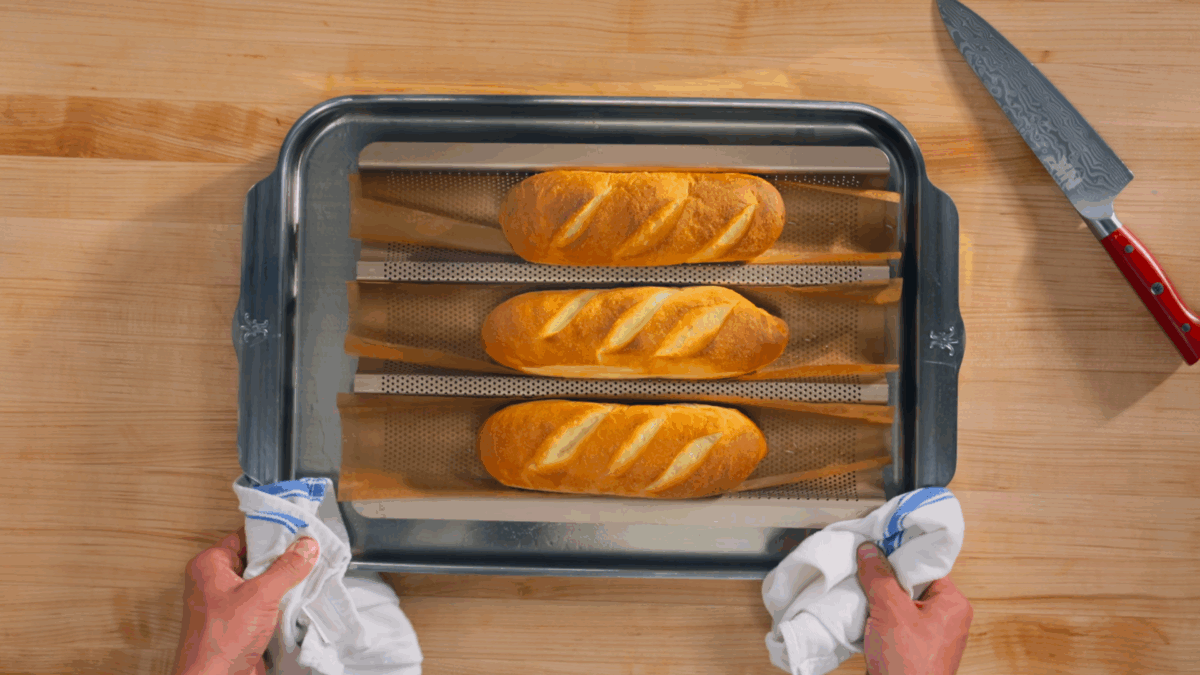 Nick DiGiovanni holding a tray with three baked banh mi  French baguettes.