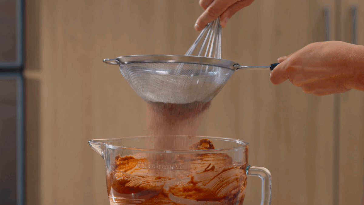 Nick DiGiovanni sifting dry ingredients into a bowl of brownie batter. 