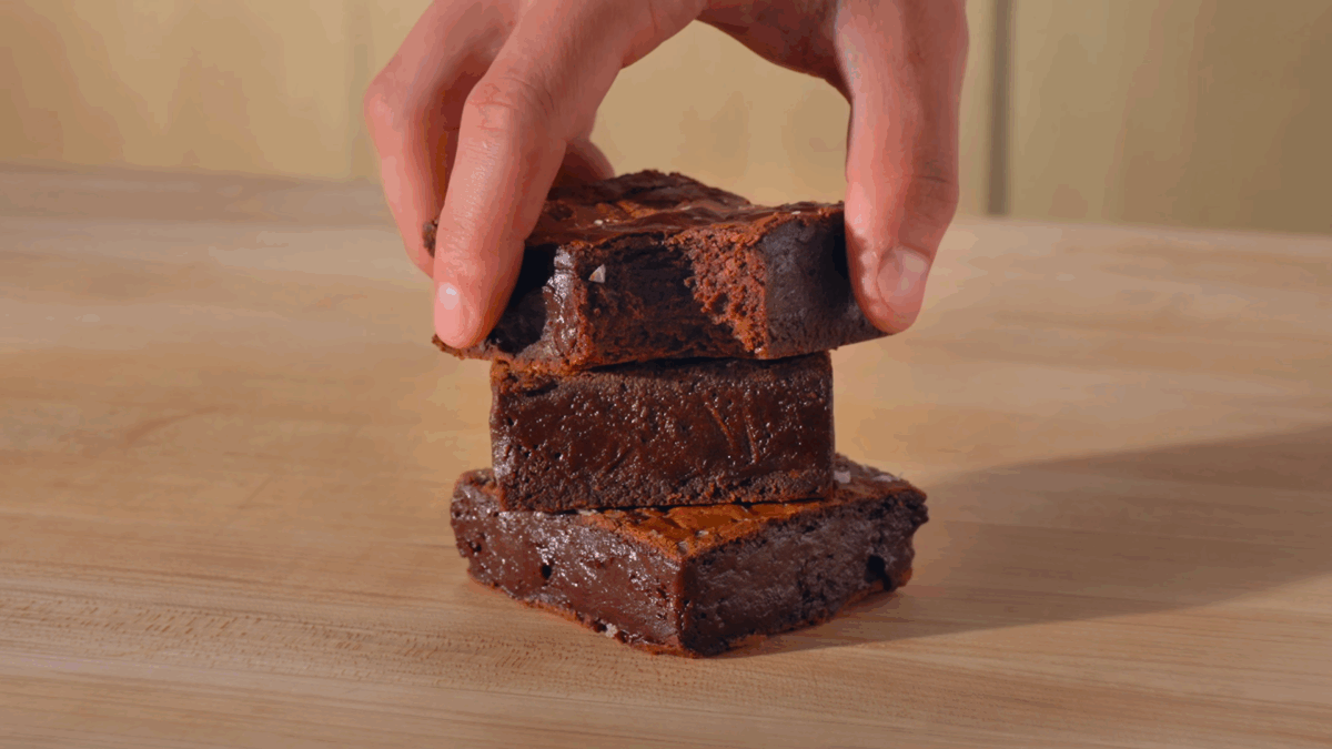 Nick DiGiovanni placing a brownie with a bite missing on top of a stack of two other brownies. 