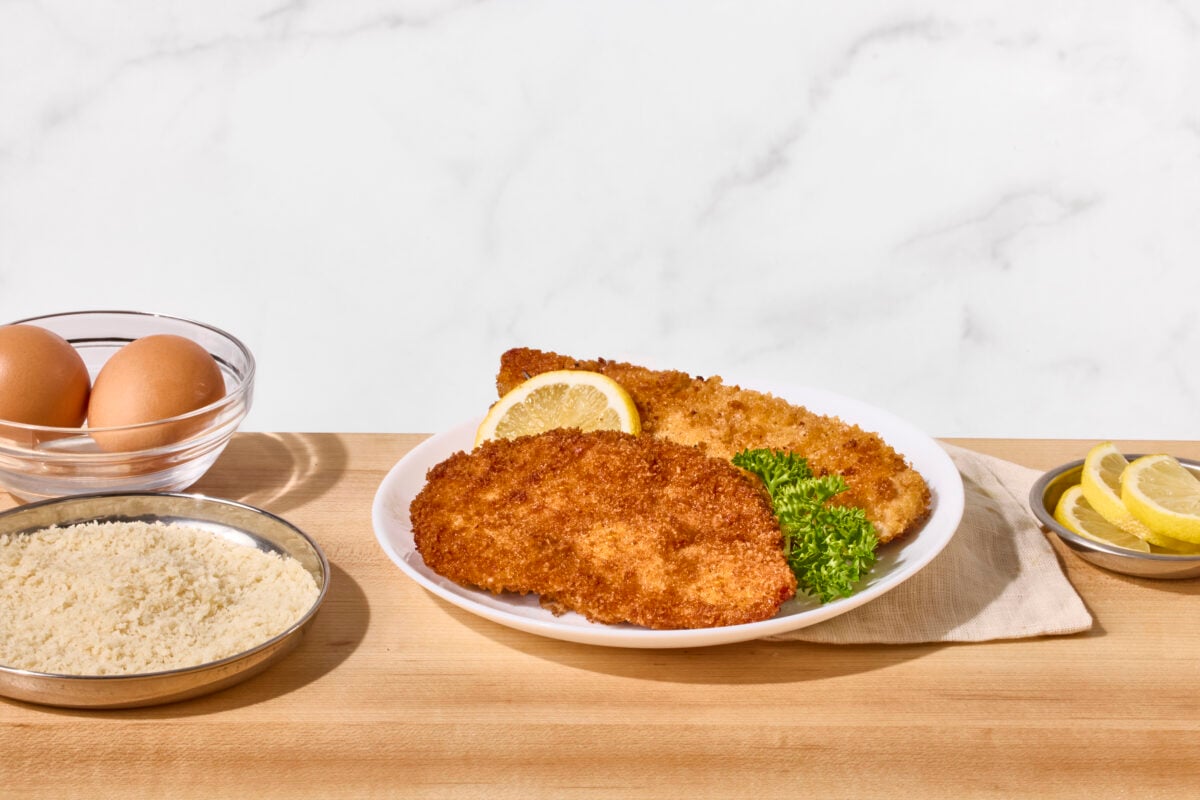 Two fried chicken cutlets on a plate with a lemon wedge.