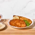Two fried chicken cutlets on a plate with a lemon wedge.