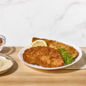 Two fried chicken cutlets on a plate with a lemon wedge.