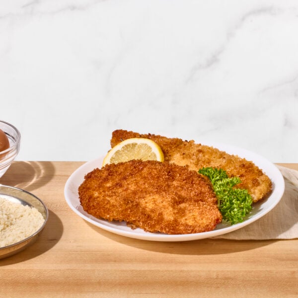 Two fried chicken cutlets on a plate with a lemon wedge.