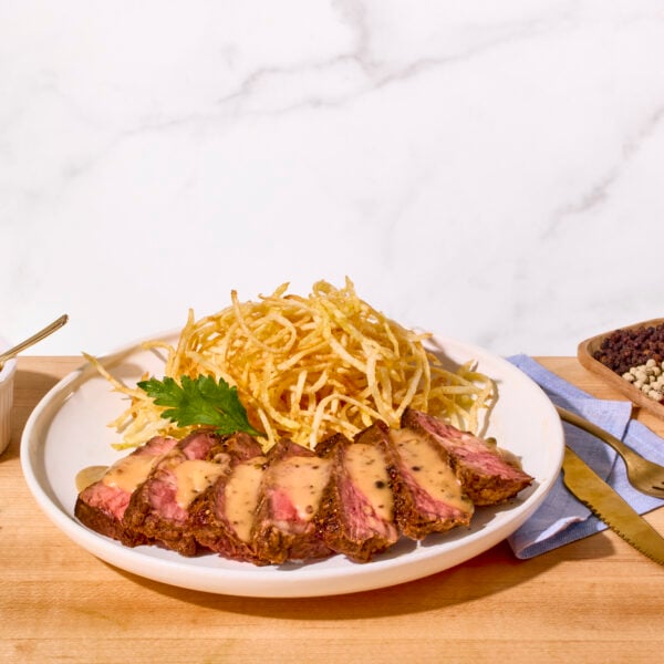 Steak au poivre sliced and plated with shoestring fries.