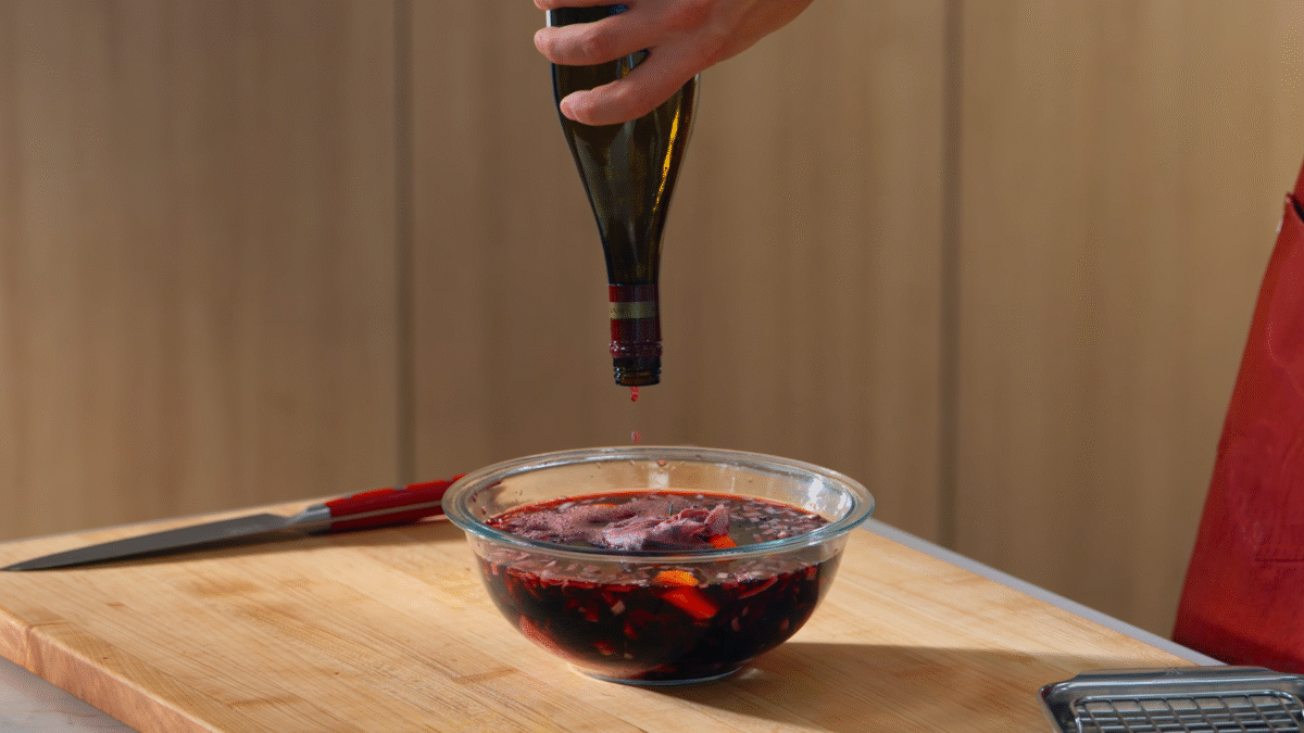 Nick DiGiovanni pouring a bottle of wine over beef chuck and vegetables in a bowl.
