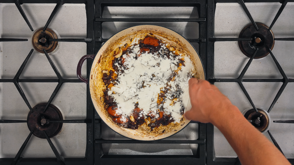 Nick DiGiovanni sprinkling flour over sautéed vegetables in a Dutch oven.